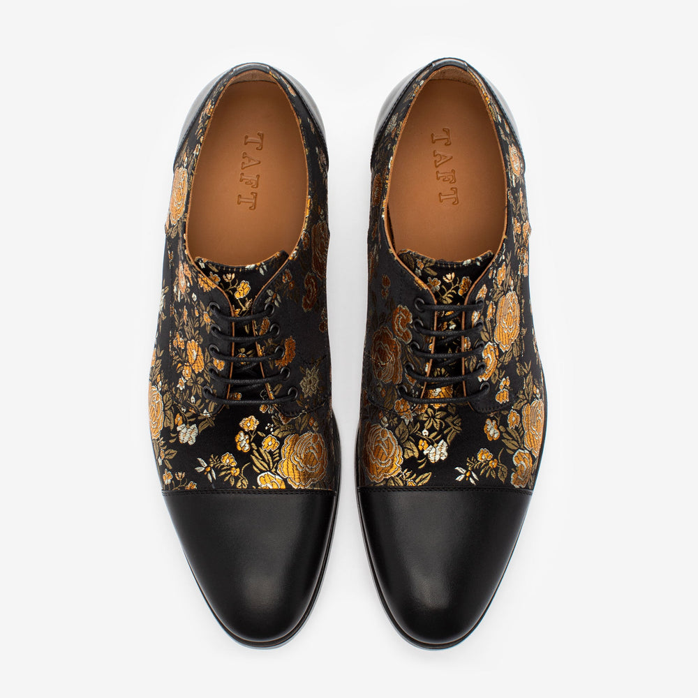 Pair of black leather lace-up dress shoes with gold and silver floral embroidery on a white background.