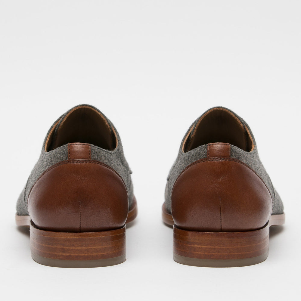 A pair of gray fabric and brown leather dress shoes viewed from the back against a white background.