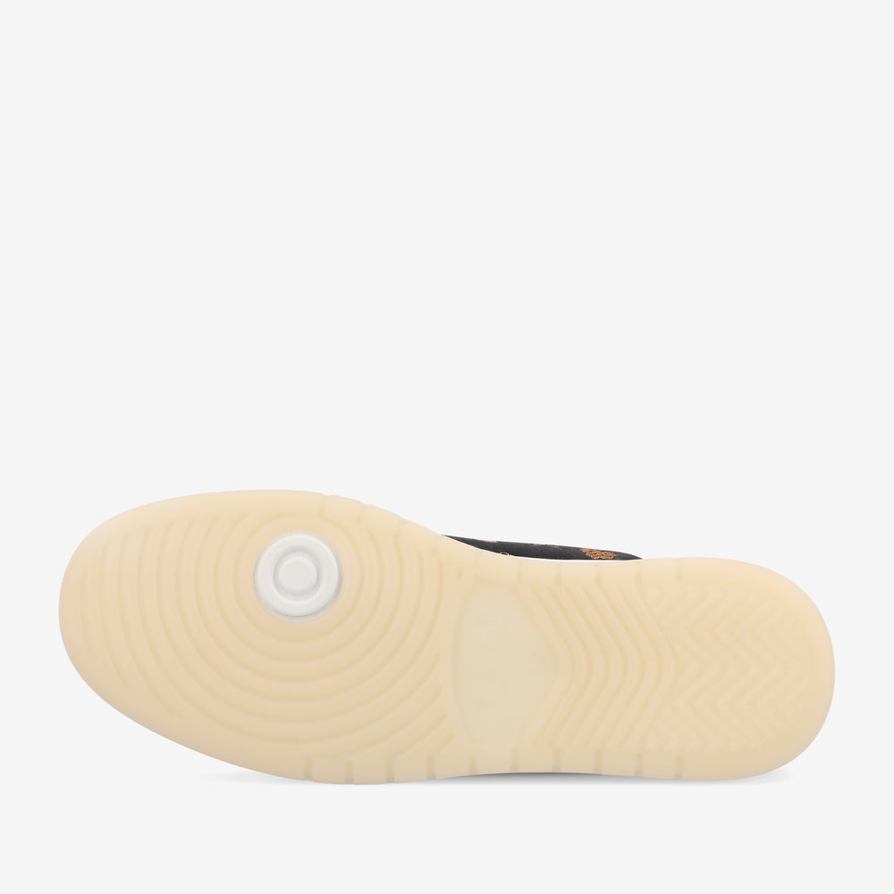 A close-up view of the sole of a shoe with a zigzag tread pattern and a circular design near the heel. The sole is light-colored.