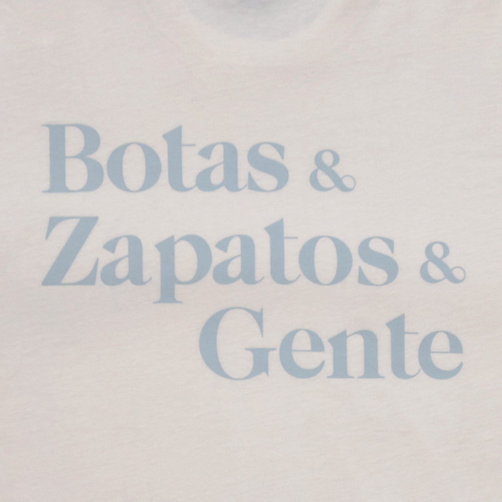 A white shirt with the text Botas & Zapatos & Gente printed in blue letters.