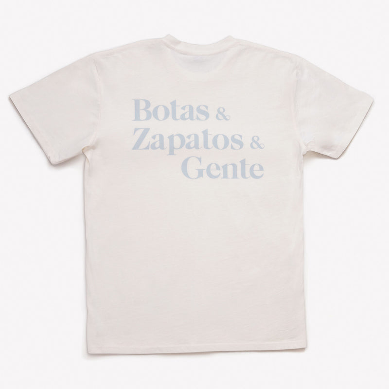 A white T-shirt with light blue text reading Botas & Zapatos & Gente printed on the back.