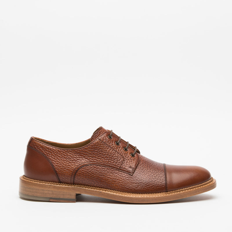 A single brown leather lace-up dress shoe is displayed against a plain white background. The shoe has a textured upper and a smooth toe cap, with a wooden sole.