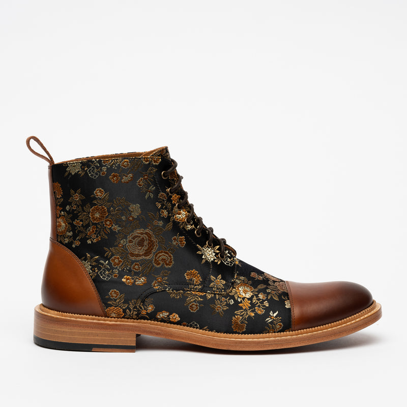 A black and brown lace-up boot with a floral pattern on the fabric part and a smooth leather toe and heel, set against a white background.