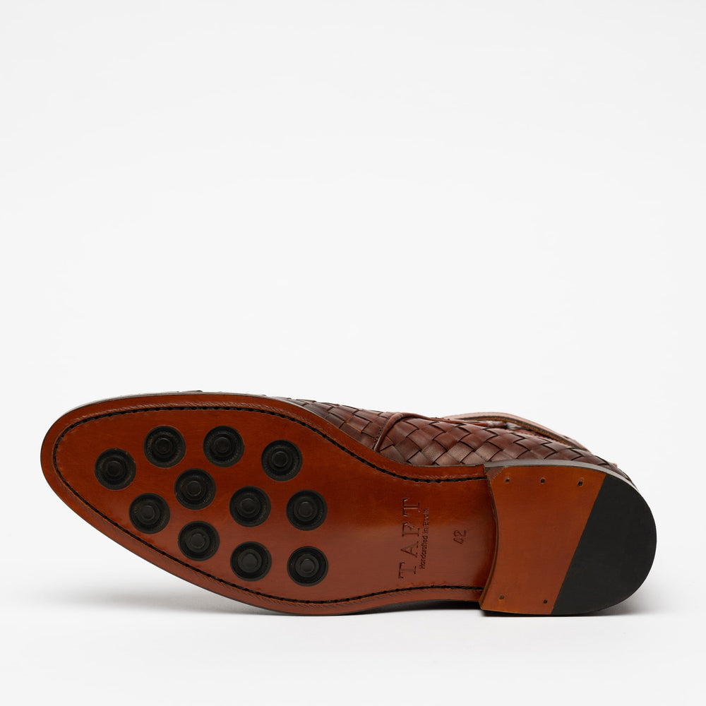 A brown shoe is shown from a bottom view, displaying a leather sole with black rubber grip inserts.