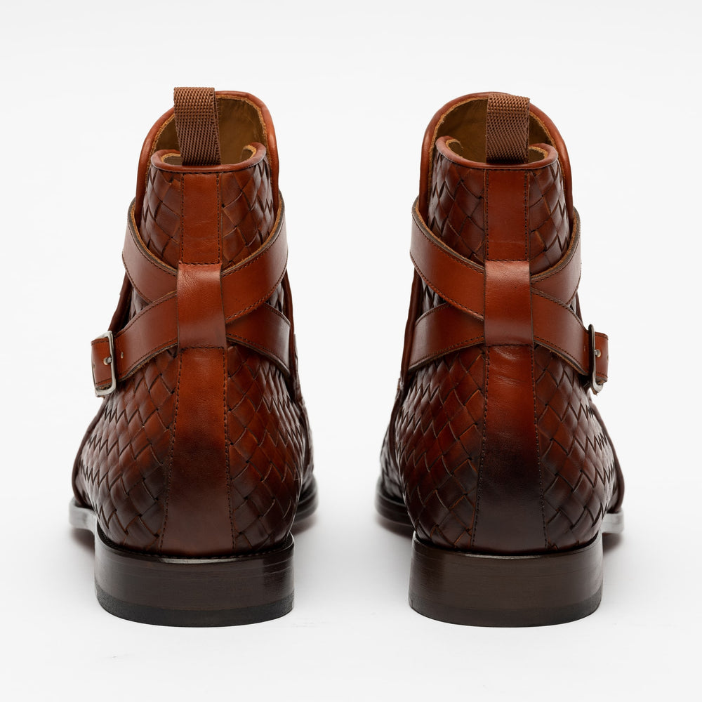 A pair of brown leather woven boots with buckles at the back, viewed from behind against a white background.