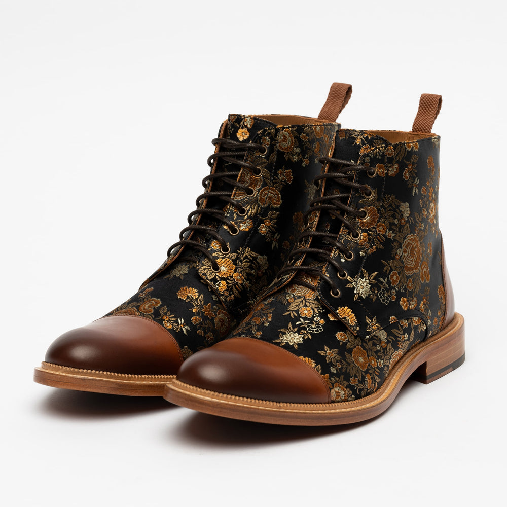 A pair of black lace-up boots with a floral print and brown leather toe caps and soles.