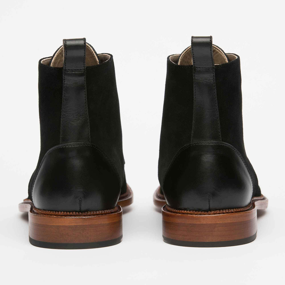 A pair of black leather boots with brown wooden soles, viewed from the back.