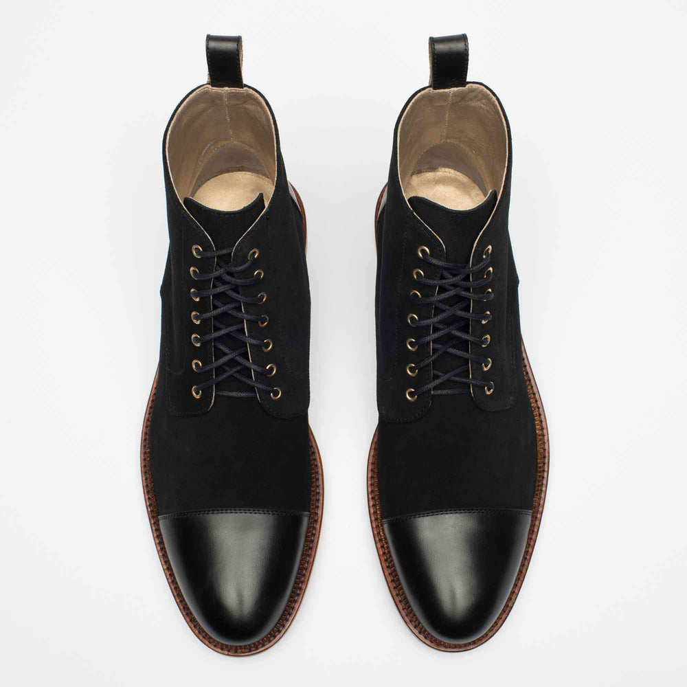 A pair of black leather boots with brown soles, featuring metal eyelets and black laces, placed side by side on a white background.