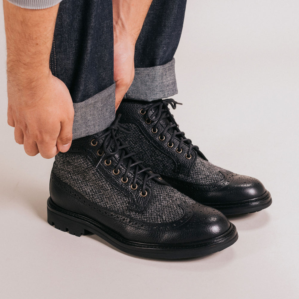 Person adjusting the cuffs of their jeans while wearing black and grey leather brogue boots.