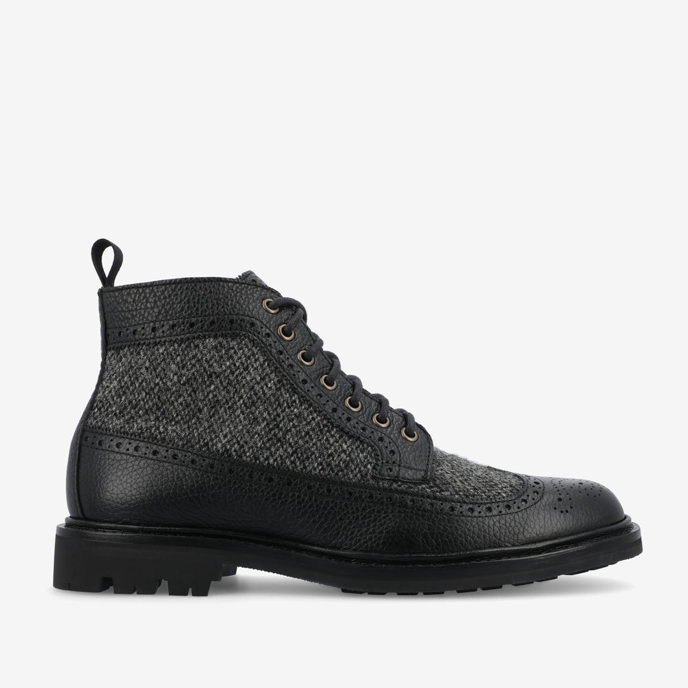 Black and grey lace-up brogue boot with textured fabric and leather upper, featuring a pull tab and lug sole.