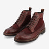 A pair of burgundy leather and suede brogue boots with intricate perforated detailing, brown laces, and sturdy soles.