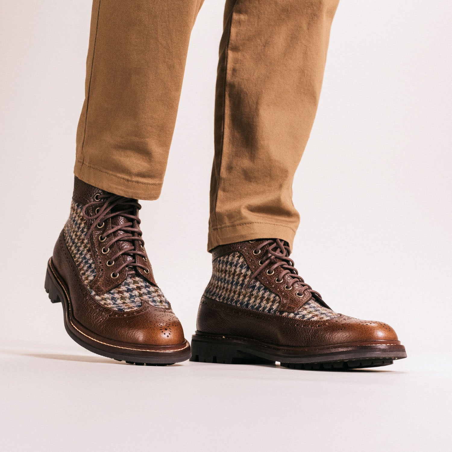 A person wearing brown leather and houndstooth pattern boots with beige pants.