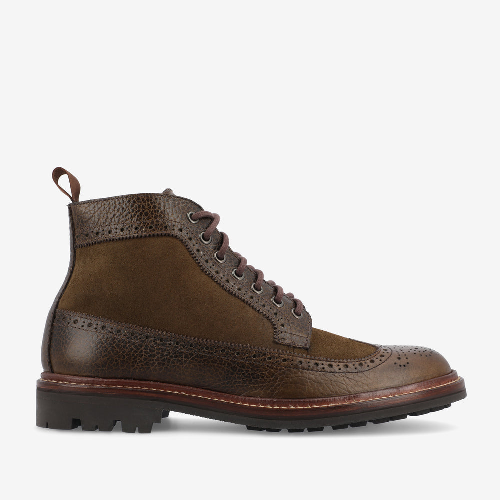 A brown leather and suede lace-up boot with brogue detailing, featuring a textured upper, pull tab, and a chunky treaded sole.