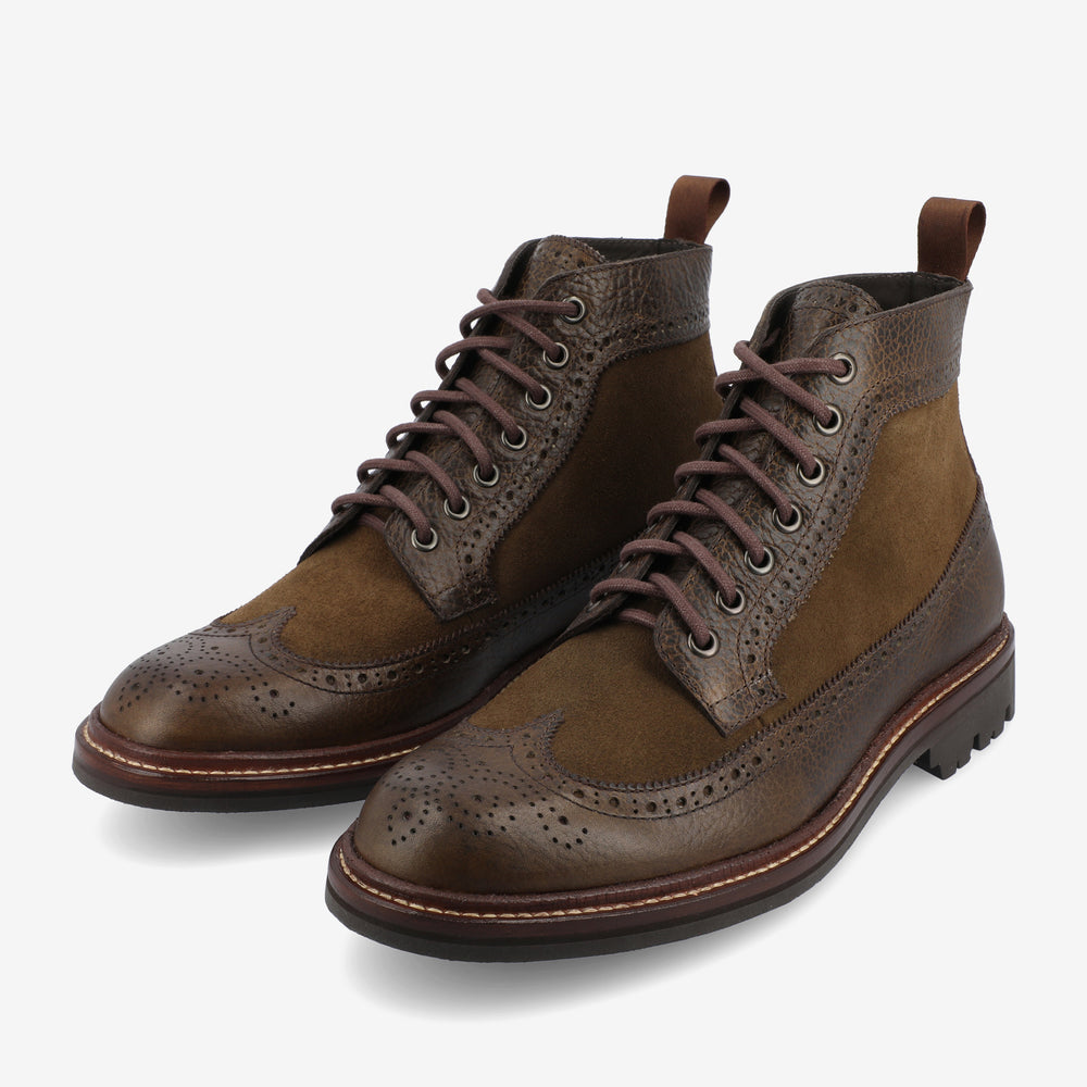 Brown leather and suede brogue boots with intricate detailing, metal eyelets, and brown laces, set against a white background.