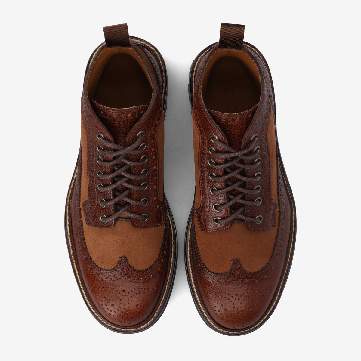 Brown leather lace-up brogue shoes with decorative perforations and contrasting textures, viewed from above on a white background.