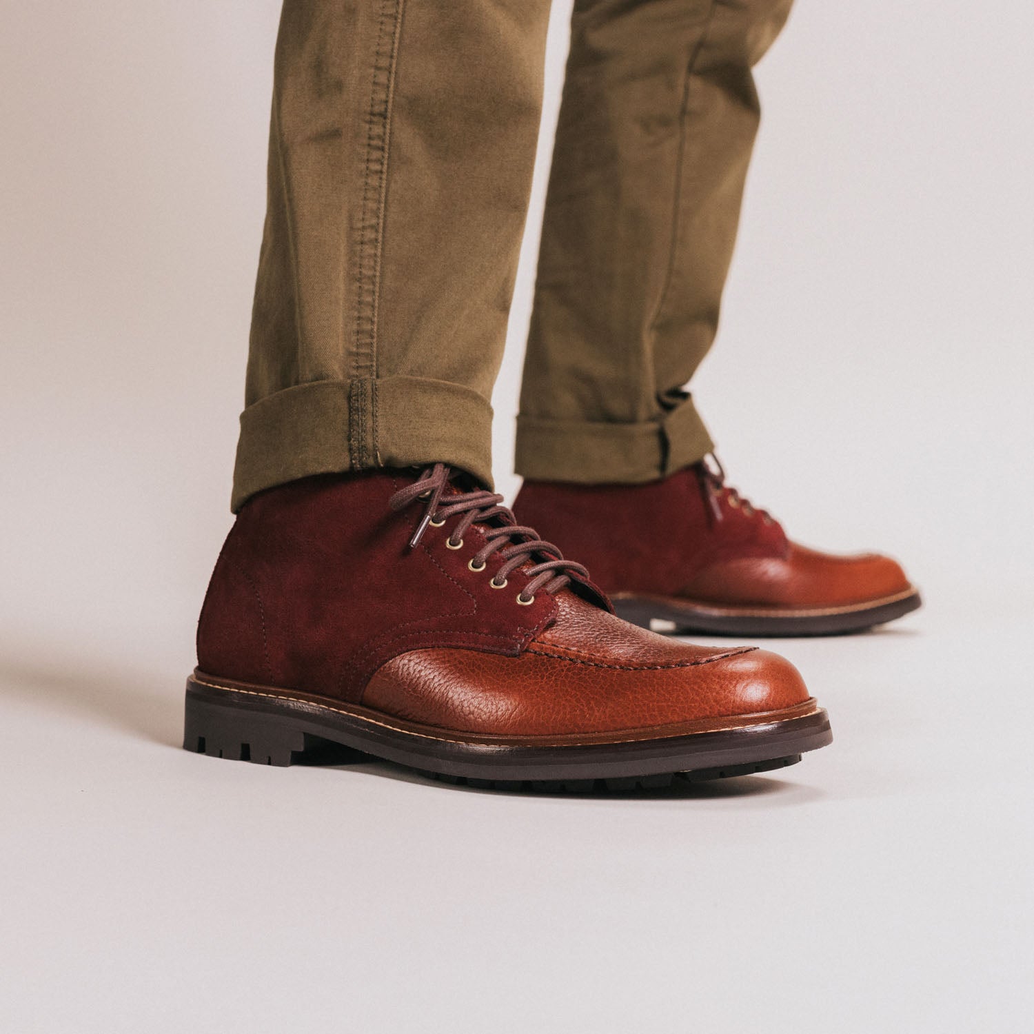 A person wearing brown leather and suede ankle boots with light brown laces, dressed in olive green pants.