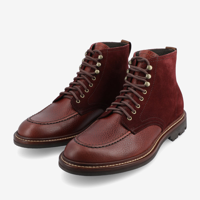 Pair of red-brown leather and suede lace-up boots with stitched detailing, metal eyelets, and a black rubber sole on a white background.