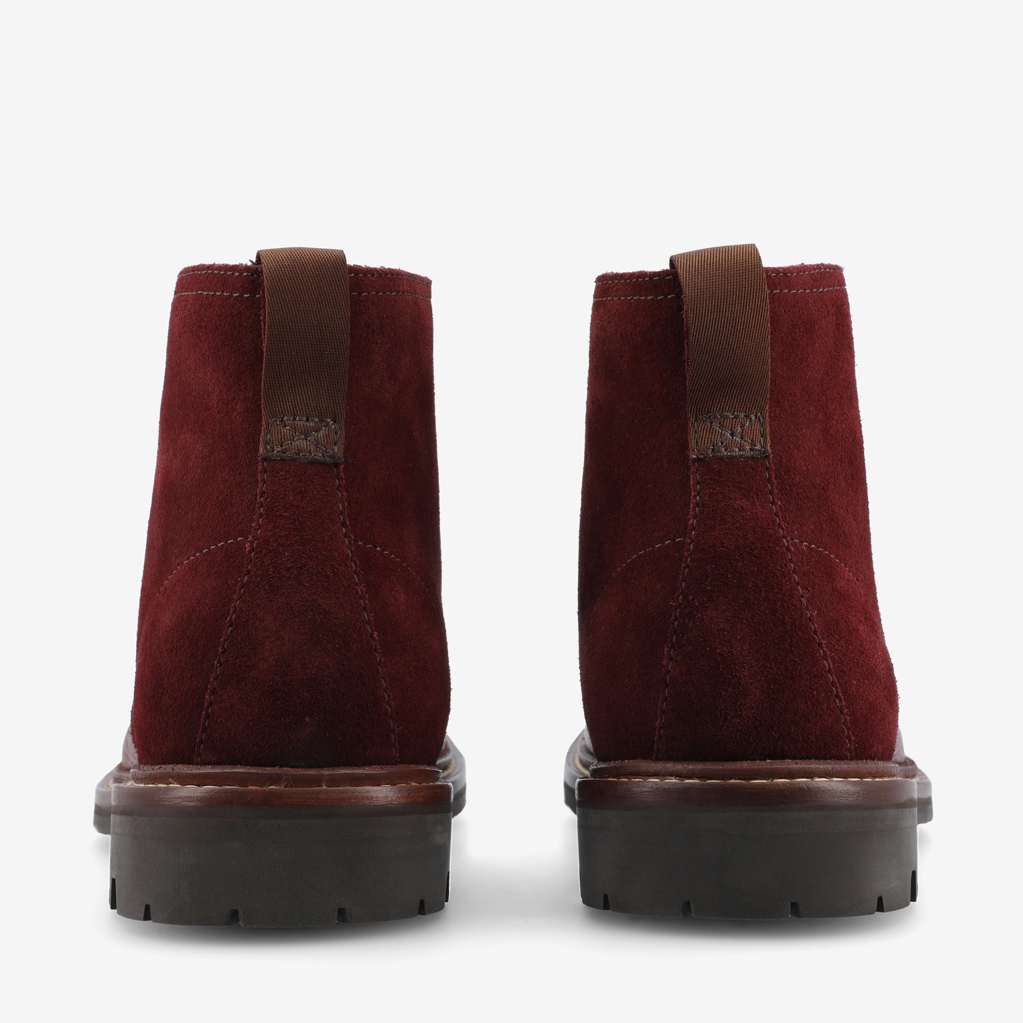 Rear view of a pair of burgundy suede ankle boots with brown pull tabs, chunky brown rubber soles, and visible stitching.