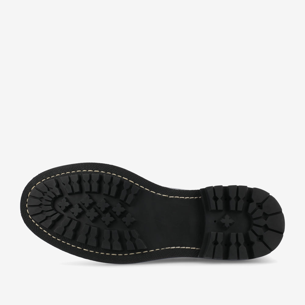 The image shows the sole of a black shoe with thick tread patterns and white stitching around the edge.