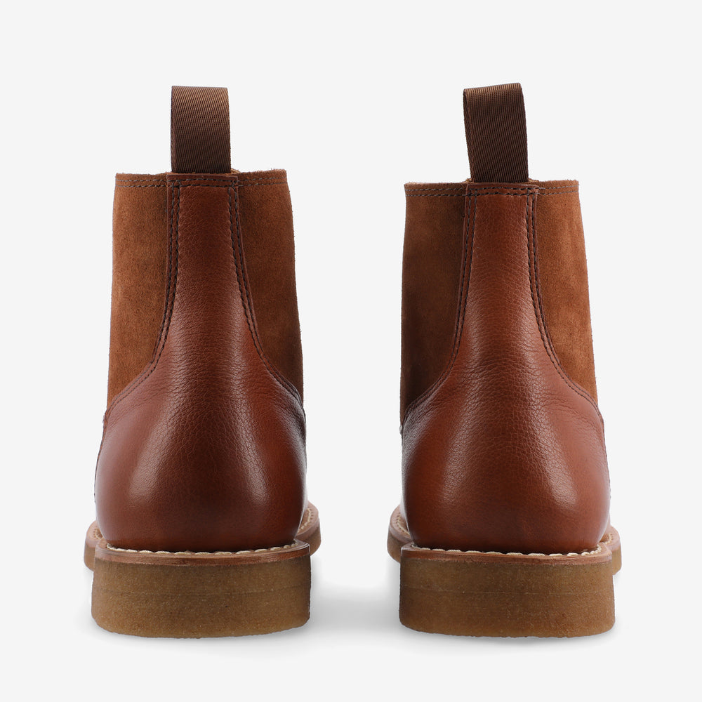 Rear view of a pair of brown leather and suede ankle boots with pull tabs and rubber soles on a white background.