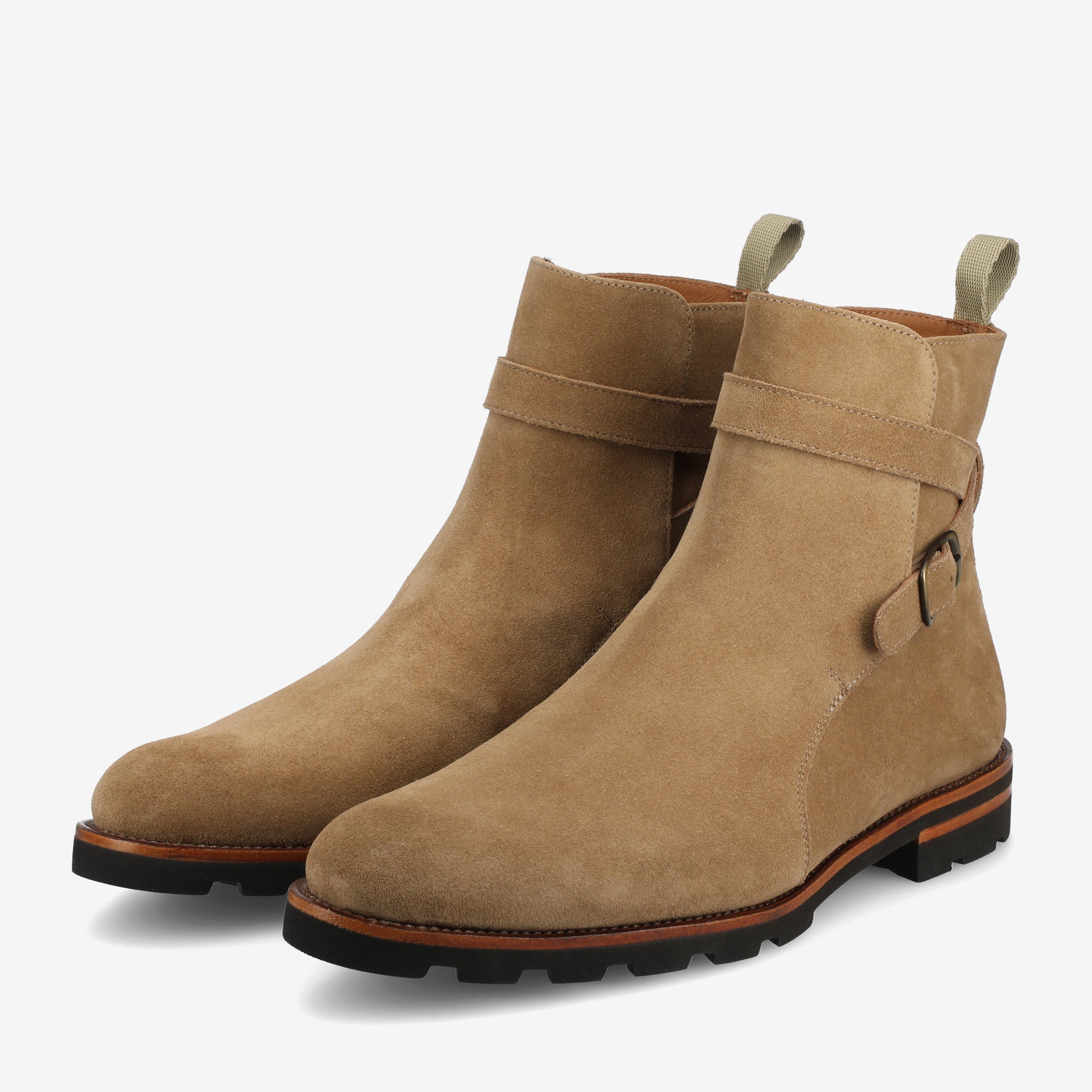 A pair of tan suede boots with a dark sole, featuring a side buckle strap and pull tabs at the back.