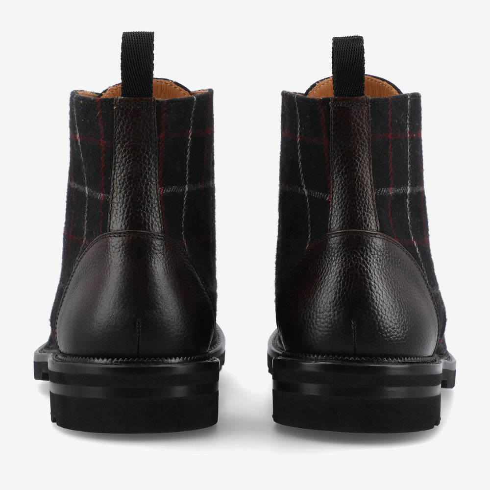 Rear view of a pair of dark brown leather and plaid fabric ankle boots with black rubber soles on a white background.