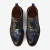 Top view of a pair of patterned navy dress shoes with intricate gold and blue designs, cap-toe style, brown soles, and blue pull tabs.