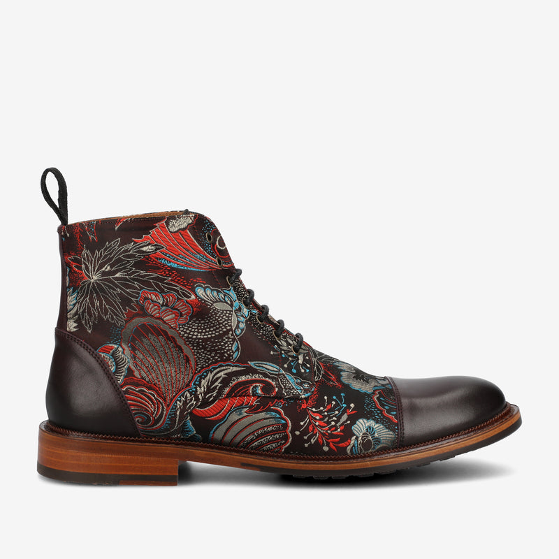 A men's boot featuring a floral pattern with red and blue accents, brown leather toe, and heel, and a light brown wooden sole.