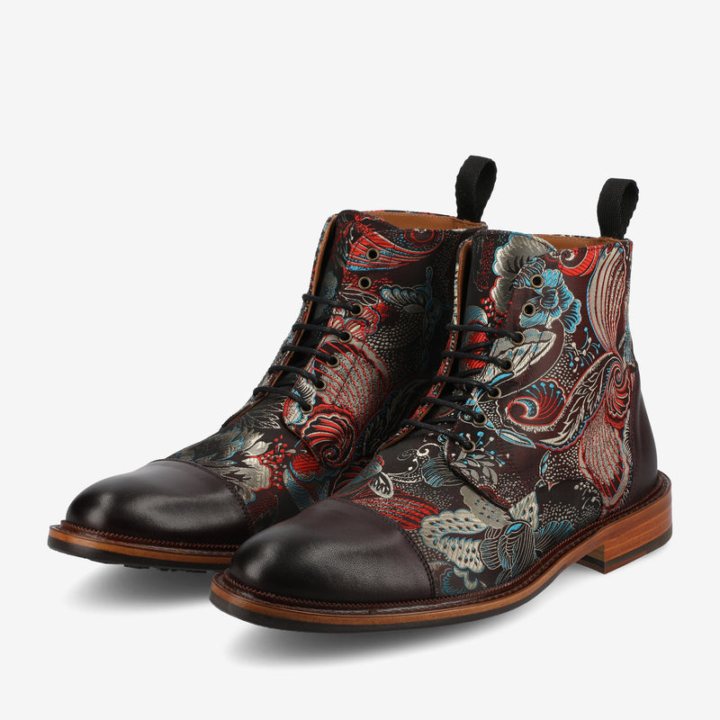 A pair of high-top leather boots with intricate multicolored patterns featuring red, blue, and cream designs, black laces, and a wooden sole.