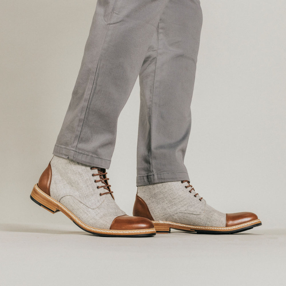 Gray pants and two-tone shoes with brown leather and gray fabric detailing on a pair of legs.