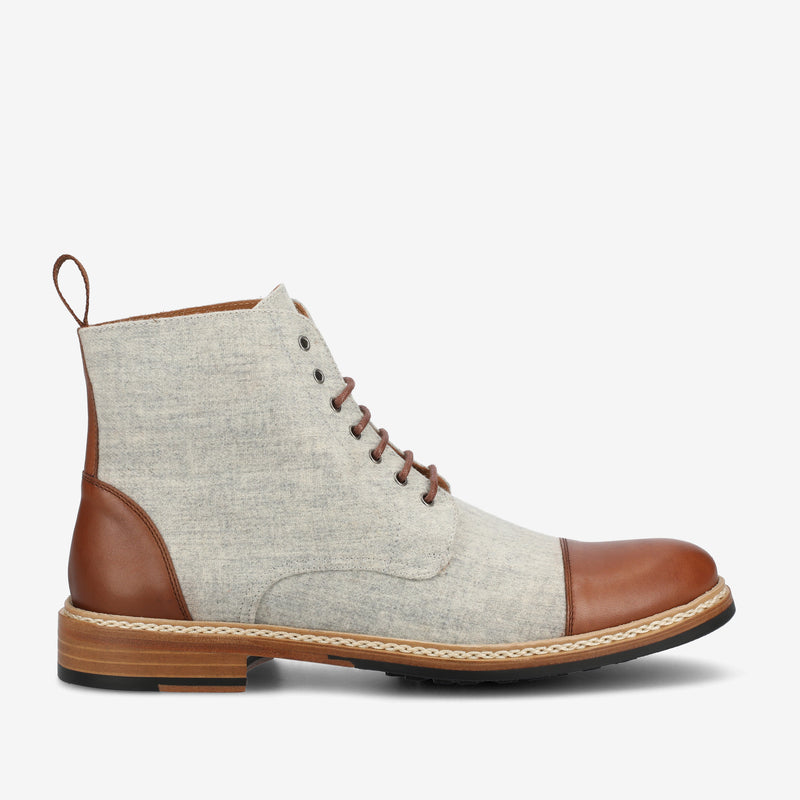 A single beige and brown lace-up boot with a wooden sole and patterned stitching detailing around the sole.