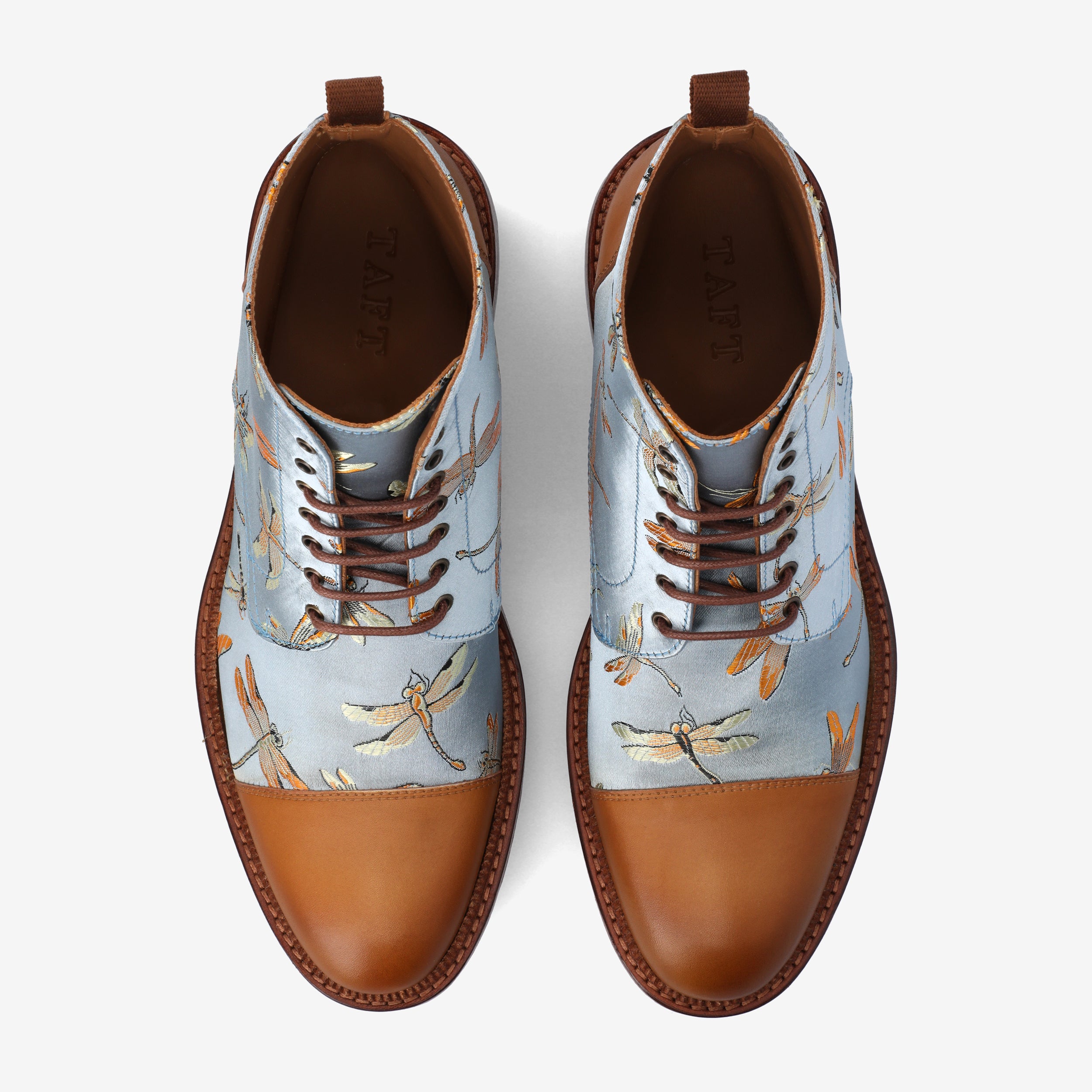 Top view of a pair of ankle-high lace-up shoes with light blue fabric featuring dragonfly patterns, gloss tan leather toe caps, brown edges, and wooden soles.