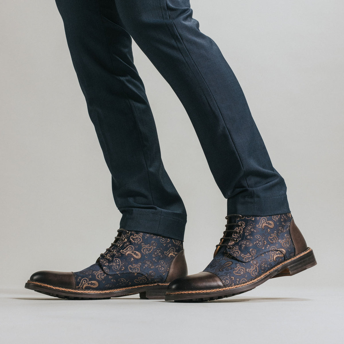 A person wearing dark blue patterned lace-up boots paired with navy blue trousers.