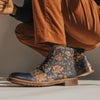 A person wearing brown pants and colorful, patterned blue leather boots is crouching down, highlighting the intricate design of the boots.