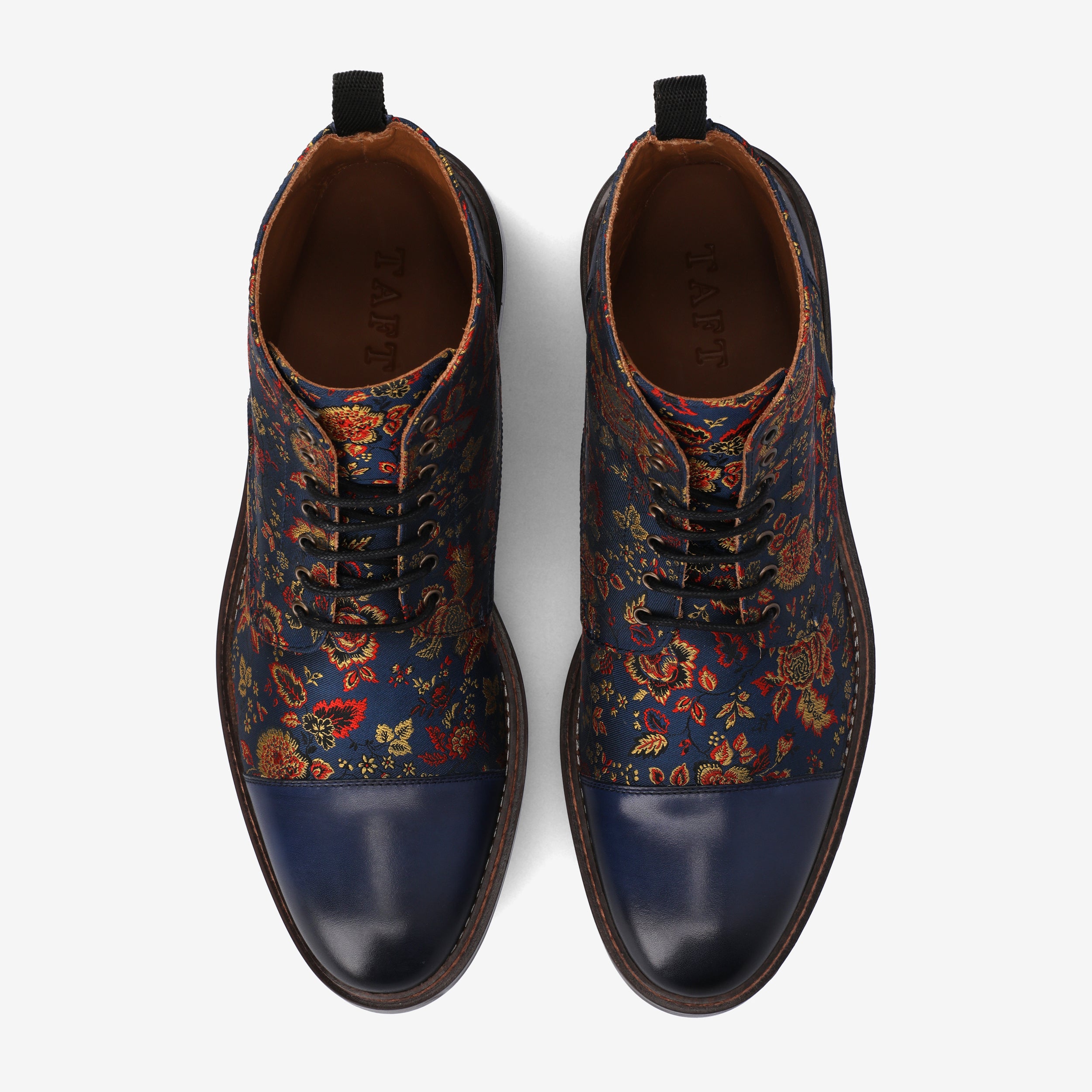 Top view of a pair of blue leather dress boots with a floral-patterned fabric design, featuring black laces and brown soles.