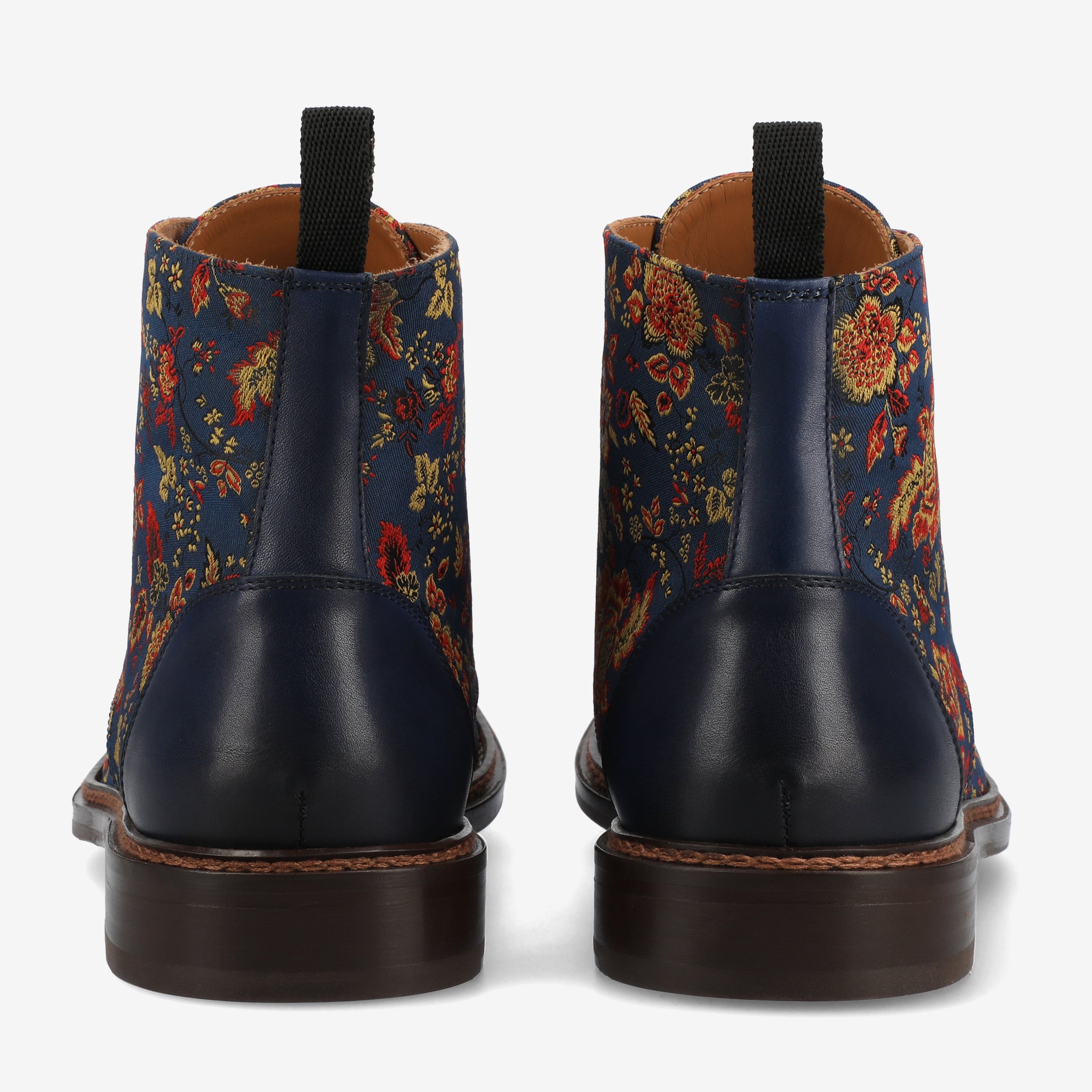 Rear view of a pair of ankle boots with a floral pattern on the fabric and navy blue leather accents, featuring brown soles and black pull tabs.