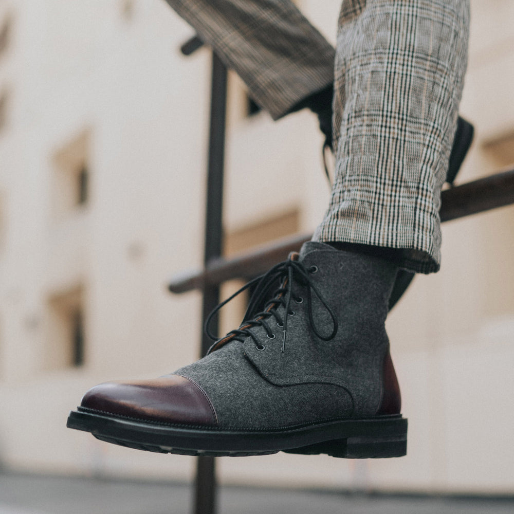 Close-up of a person wearing gray and brown leather lace-up boots and plaid pants outdoors.