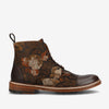 A brown leather ankle boot with a floral pattern, lace-up front, and a pull tab at the heel. The sole is light brown with a decorative stitching detail.