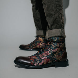 A person wearing brown corduroy pants stands in floral-patterned lace-up boots with dark brown leather accents.