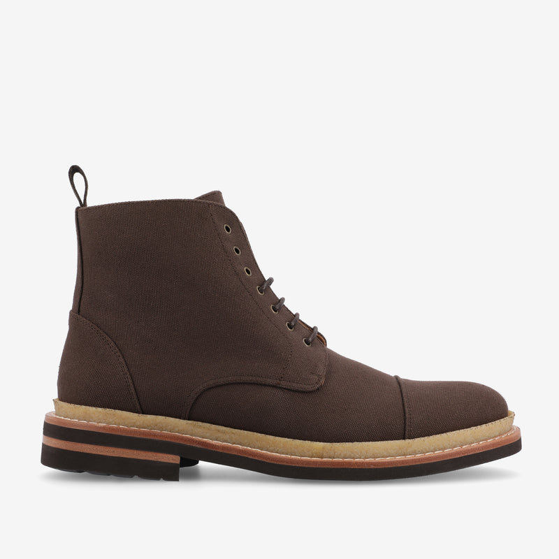 Image of a brown high-top boot with lace-up closure, leather accents, and a thick rubber sole with a layered design. The boot has a pull-tab at the heel.