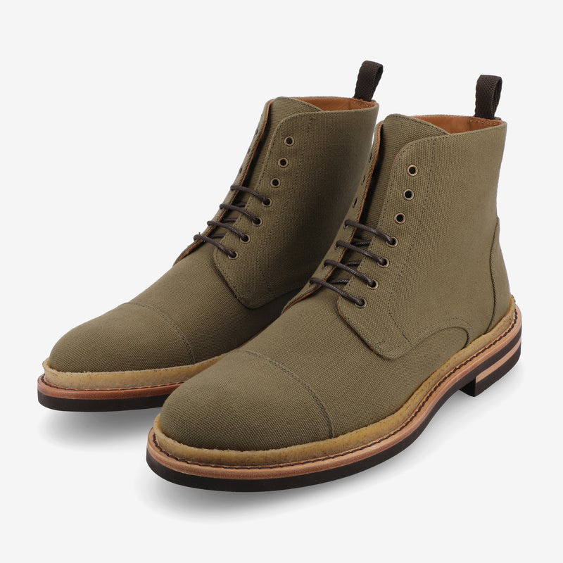 A pair of olive green canvas lace-up boots with brown soles and black laces on a white background.