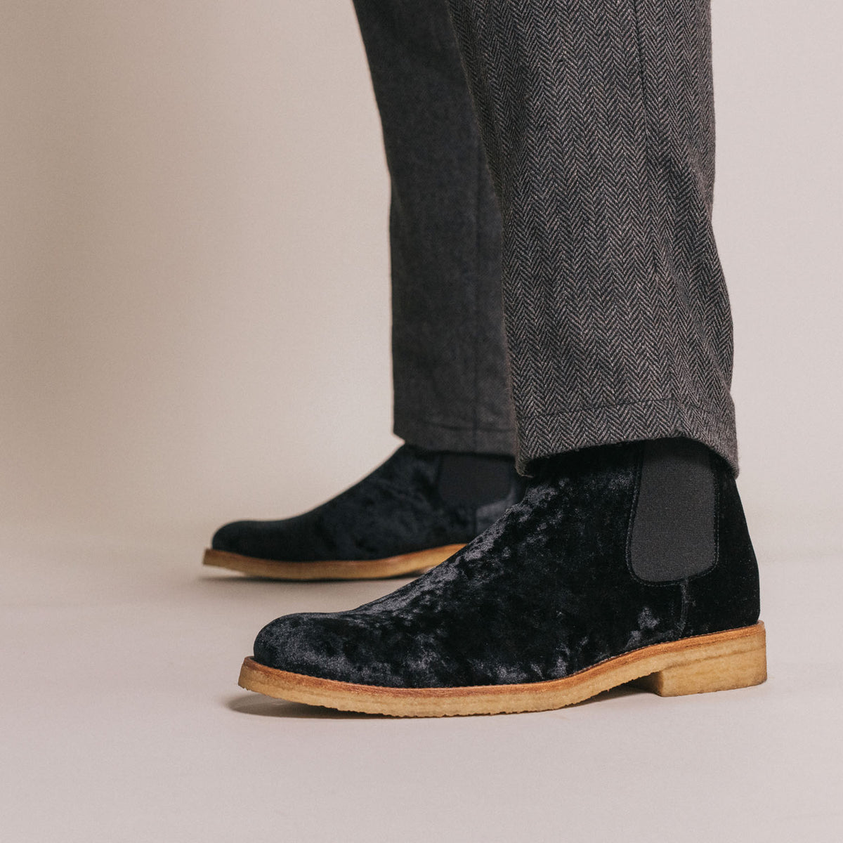 Man wearing grey herringbone patterned pants and black velvet ankle boots with light brown soles.