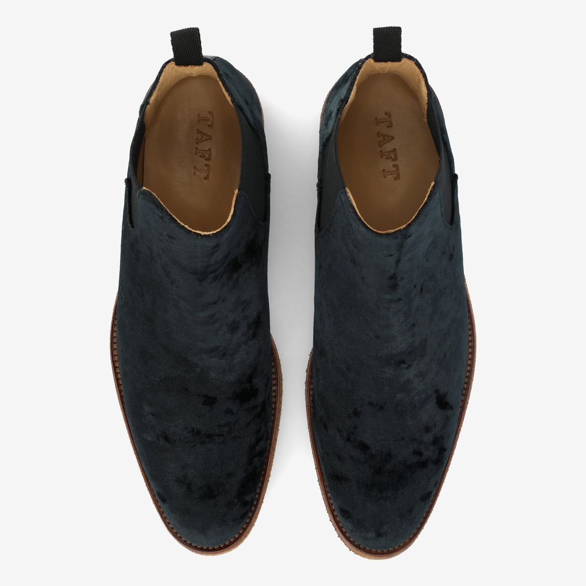 Top view of a pair of dark blue, velvet-textured slip-on dress shoes with brown soles and the word TAFT inscribed inside.