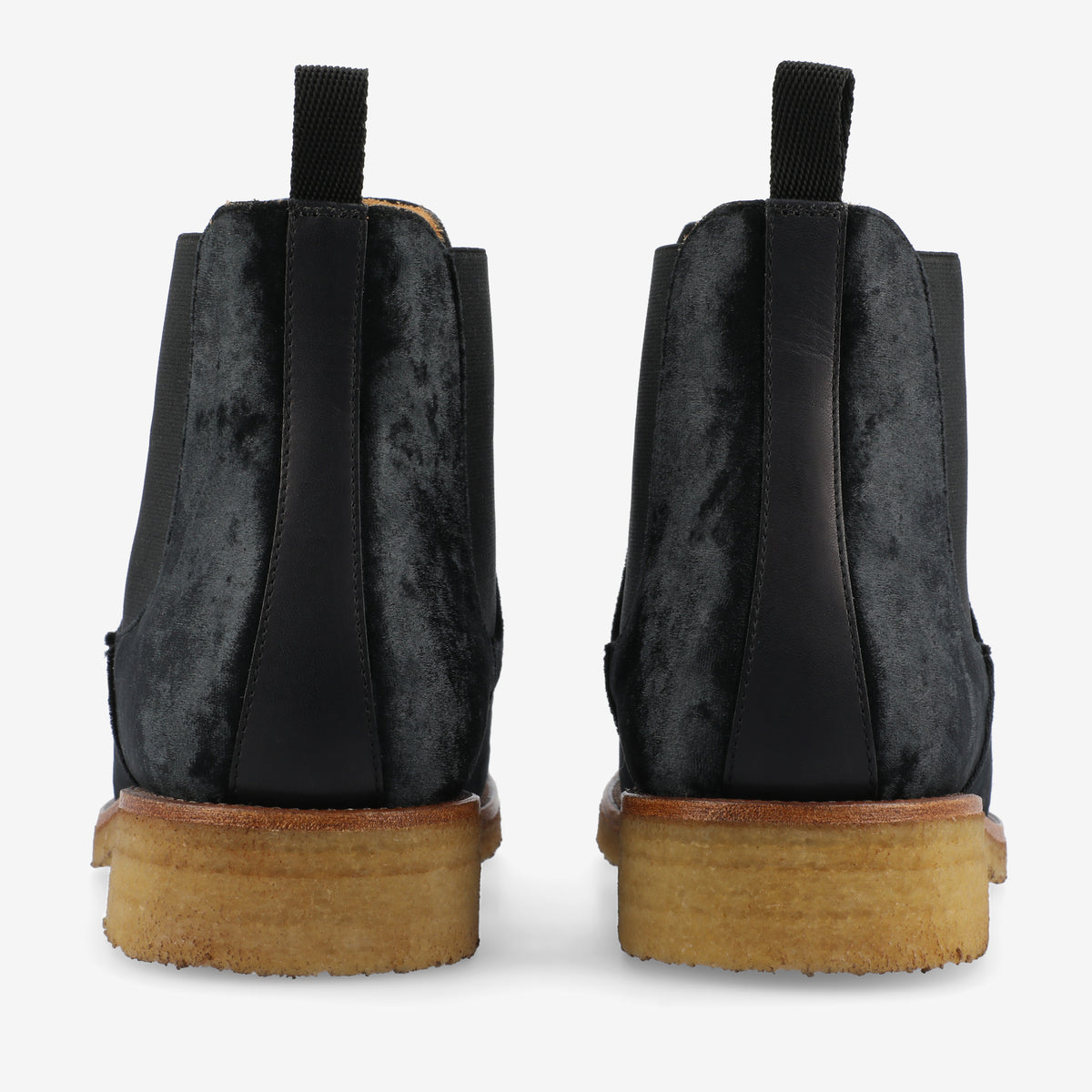 Back view of a pair of black suede Chelsea boots with elastic side panels and beige crepe soles.