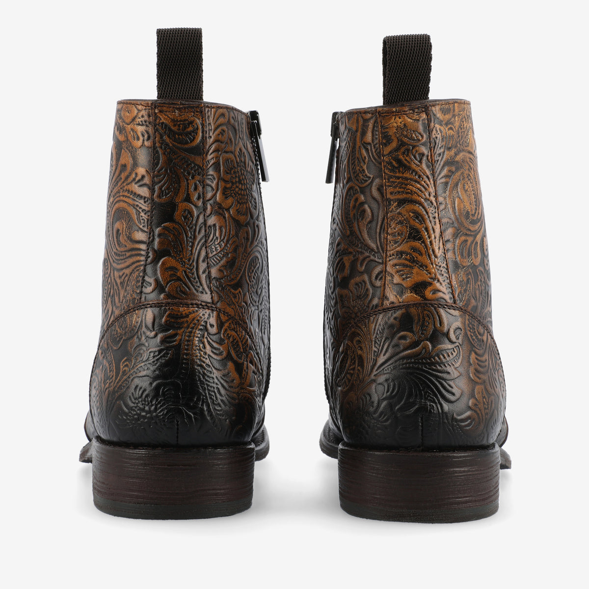 Back view of a pair of brown leather boots with intricate embossed patterns, black pull tabs, and dark brown soles.