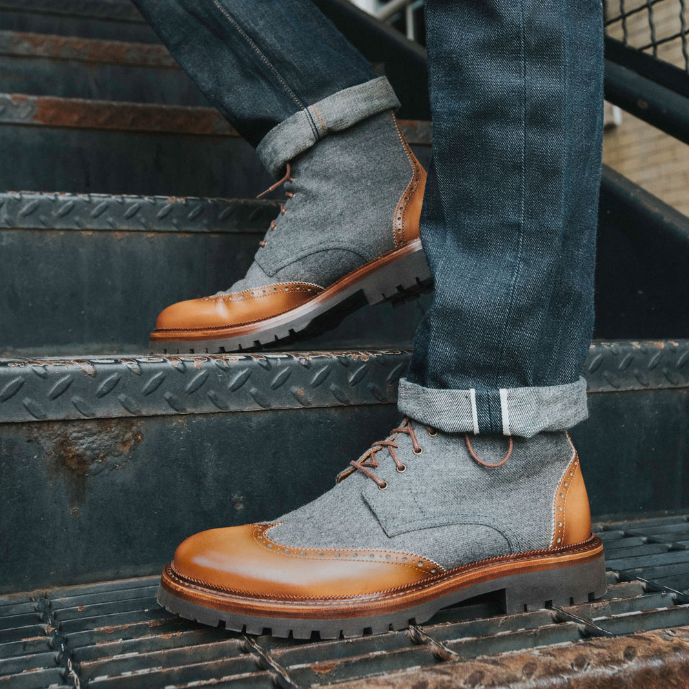 Close-up of a person wearing grey and brown leather boots and rolled-up jeans standing on metal stairs.