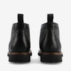 Back view of a pair of black leather and fabric ankle boots with pull tabs on a white background.