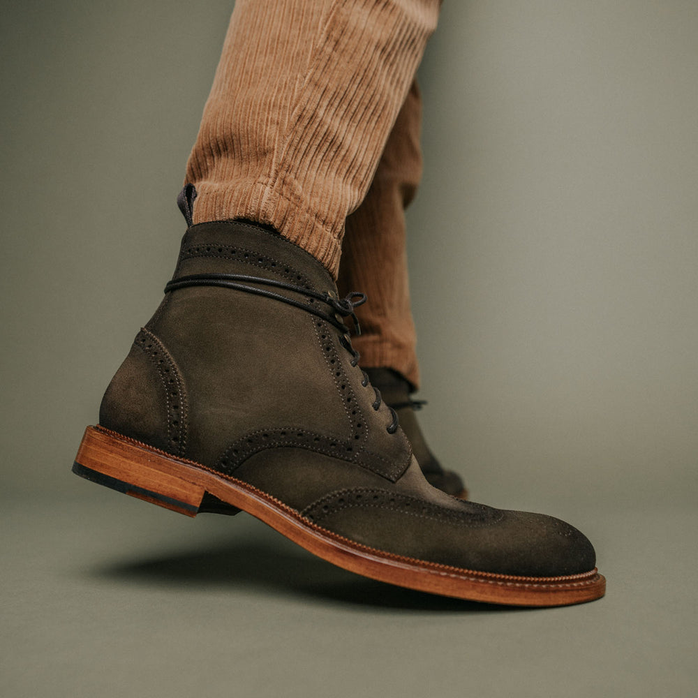 A close-up of a person wearing dark brown suede brogue boots and tan corduroy pants.