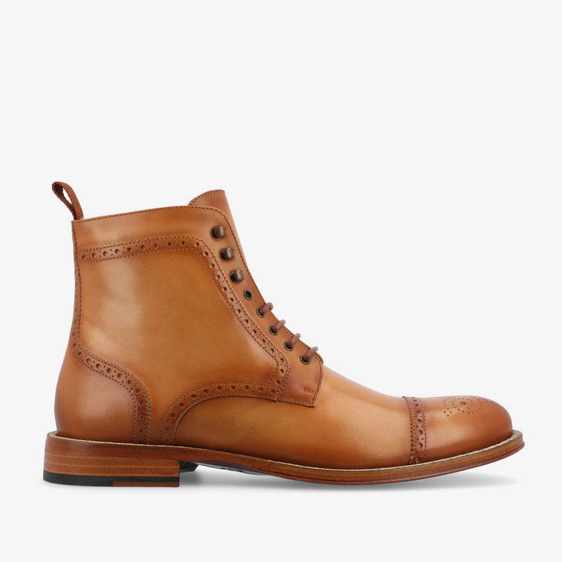 A single tan leather boot with brogue detailing, a round toe, and brown laces.