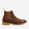 Side view of a brown Chelsea boot with a suede finish, leather toe cap, elastic side panels, pull tab at the back, and a rubber sole with a natural crepe texture.